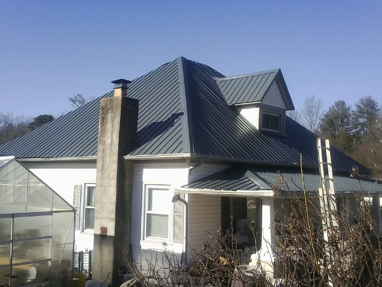 Dark blue standing seam metal roof on a white farmhouse with dormer — Slate & Tile Roof Repair by Roofing Brothers in Alpine