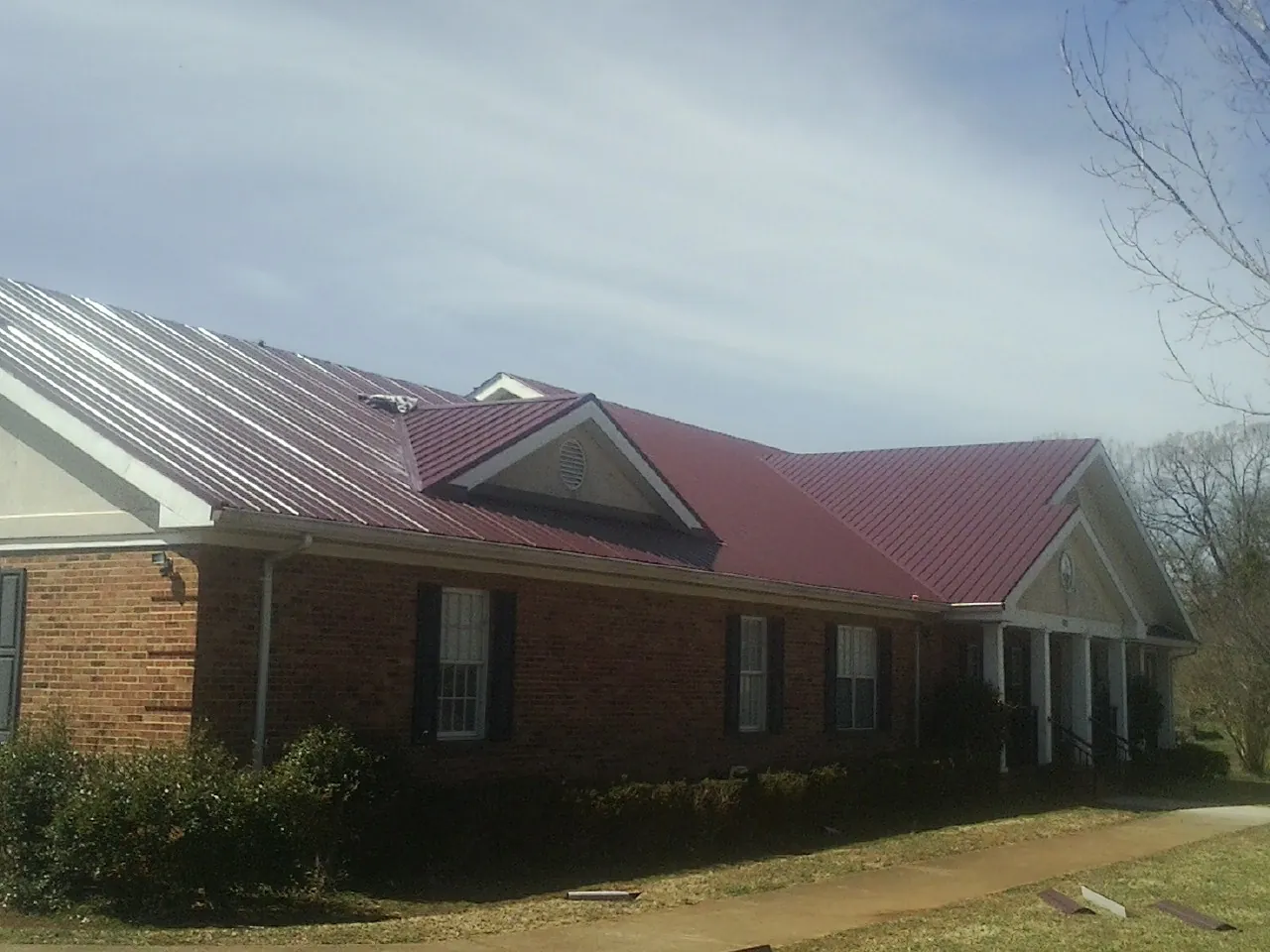 Red metal roof with gabled entries on a long brick building, from a Hail Damage Roof Repair job in Alpine